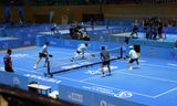 Players competing with paddles and a yellow pickleball on a blue outdoor court