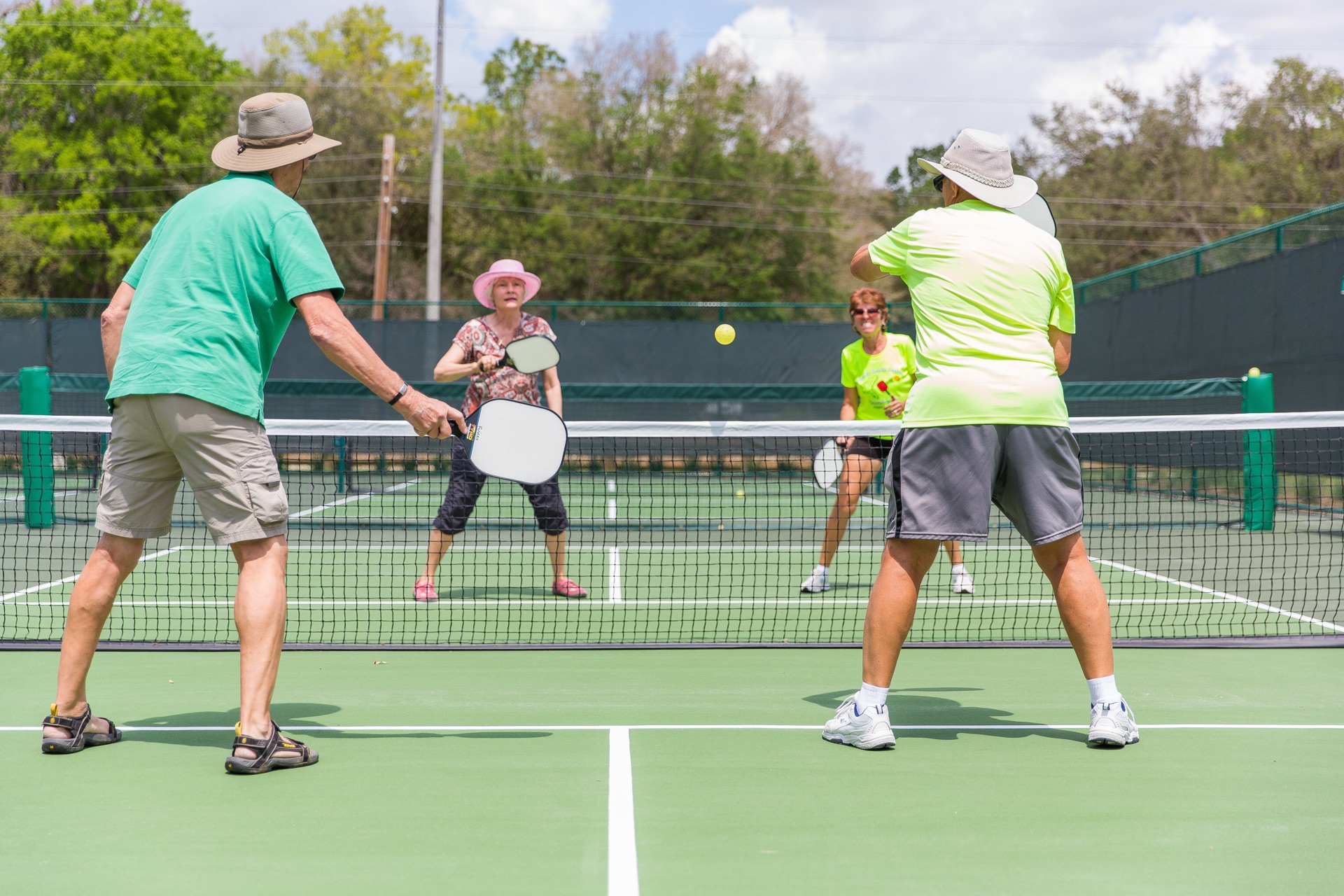 Four recreational players in a doubles rally on an outdoor pickleball court
